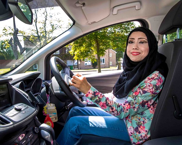 Nazmin is sat in the driving seat of her car with her hands on the specially adapted steering wheel