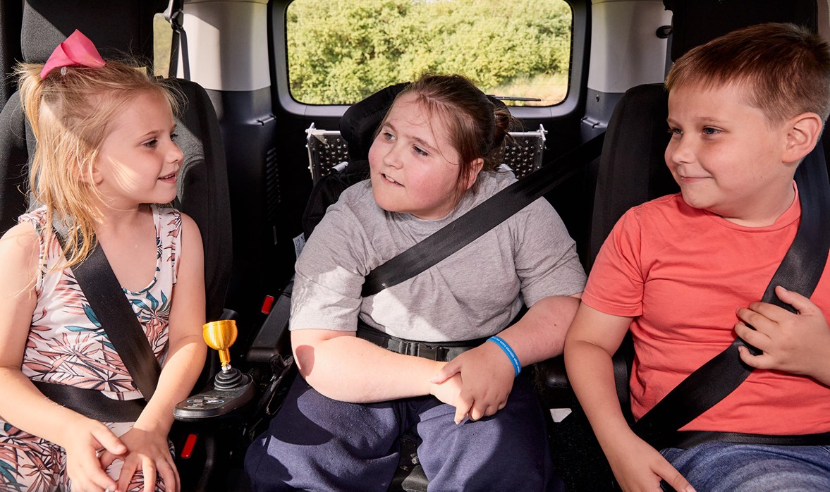 Three children sit in the back of a wheelchair accessible vehicle