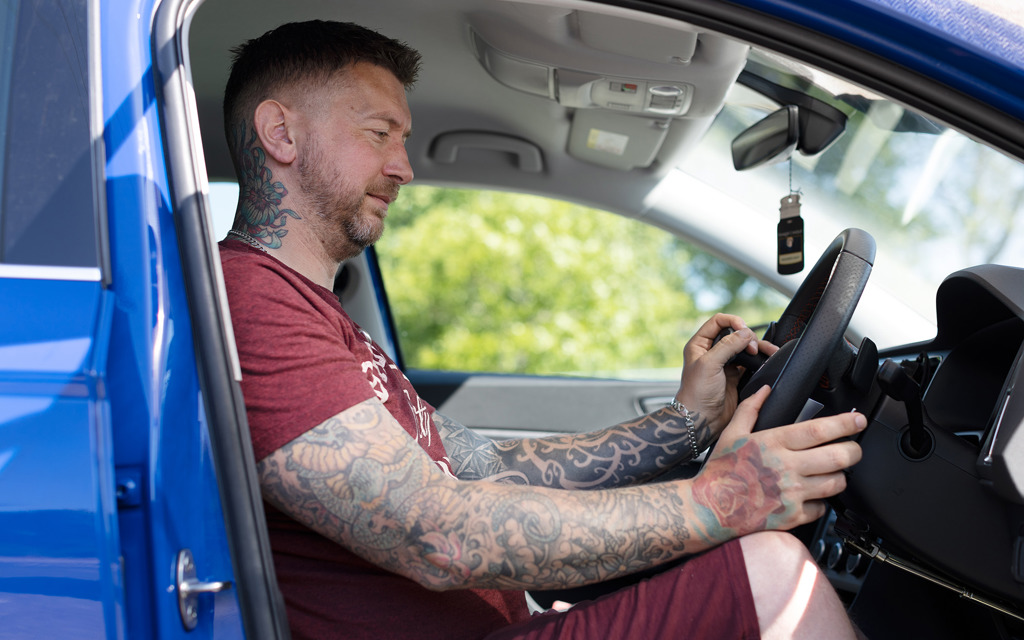 A man sitting in the driver's seat of a car holds hand controls