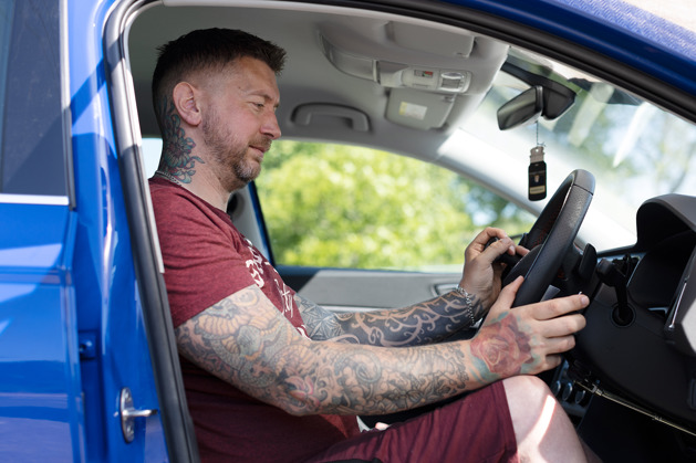 A man sitting in the driver's seat of a car holds hand controls