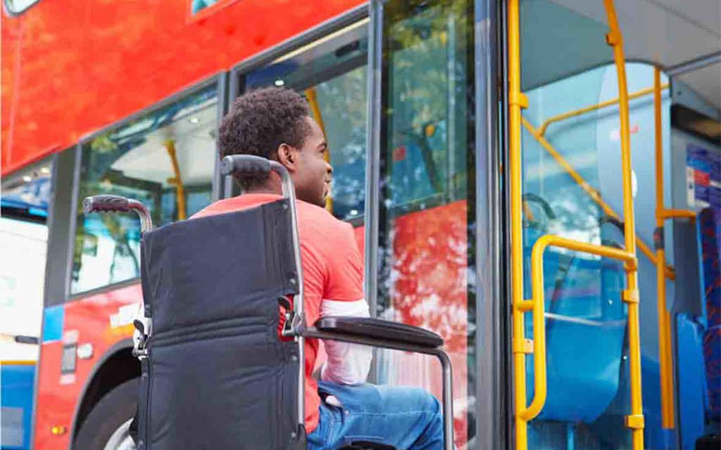 A man is sitting in a wheelchair in front of a bus. 