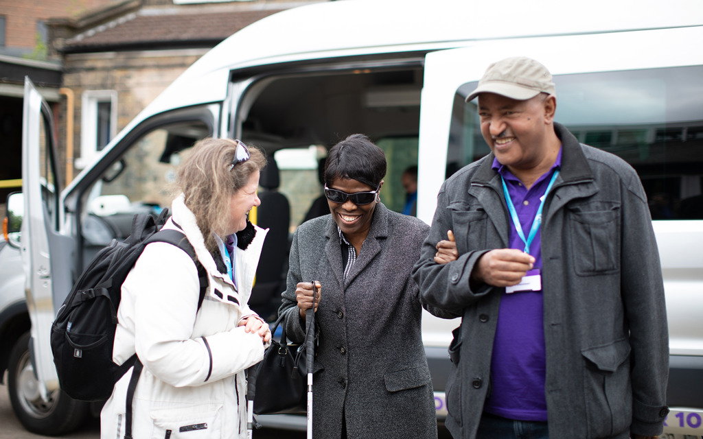 A man and a woman support another woman to get off a minibus.