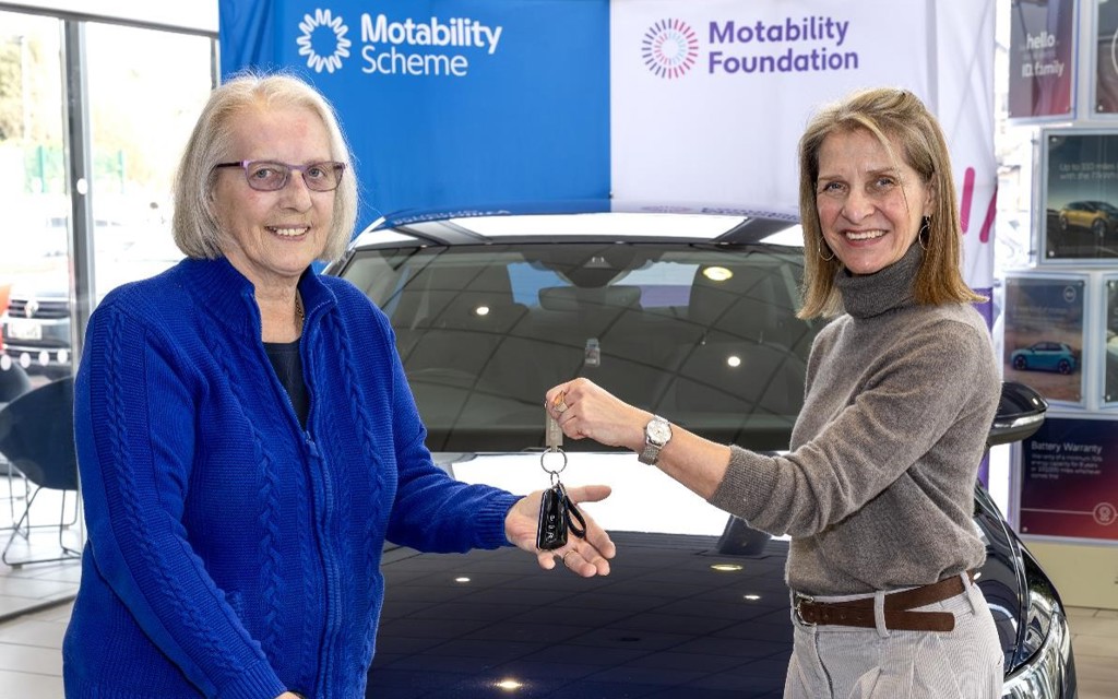 Wera Hobhouse MP presents keys to Rose at car handover in Bath. Rose's car is behind them. Rose is on the left-hand side in the photo she has white hair in a bob with glasses. She is wearing a midnight blue zip up jumper. Wera is on the left-hand side of the photo with shoulder length blonde brown hair and a grey turtleneck jumper. They are smiling looking at the camera. 