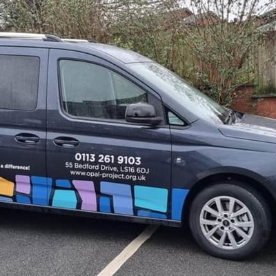 An image of OPAL's wheelchair accessible vehicle. The vehicle is black and has their logo and telephone number on the side.