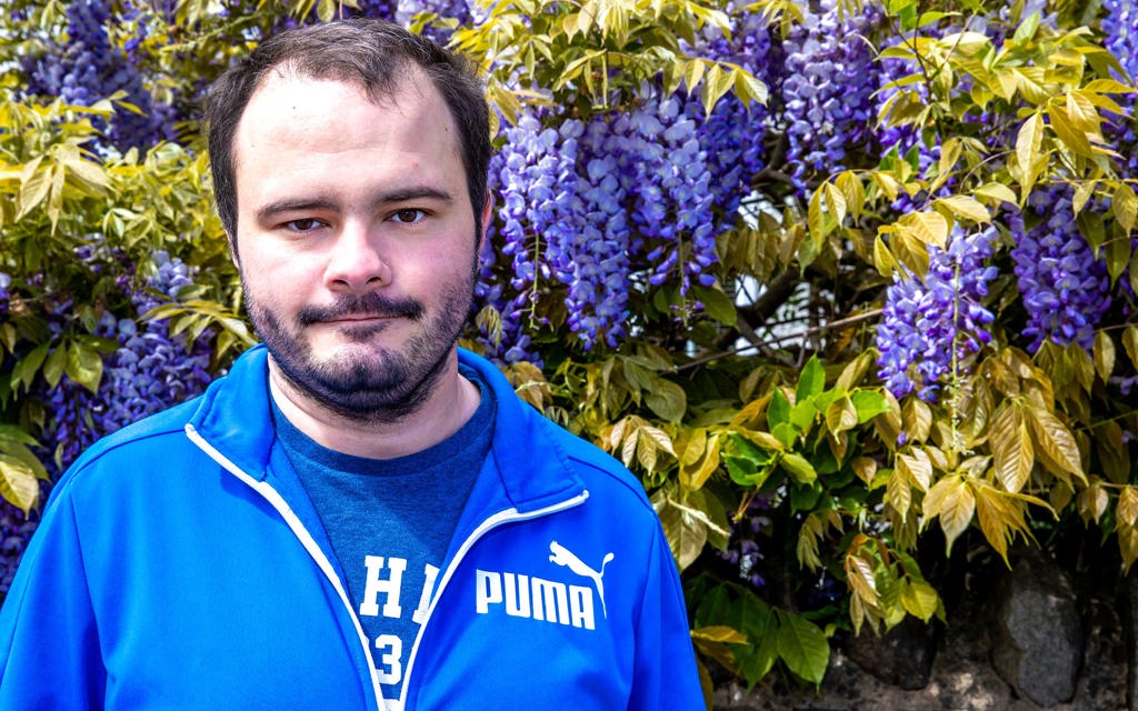 A gentleman is standing in front of a tree with large purple flowers. 