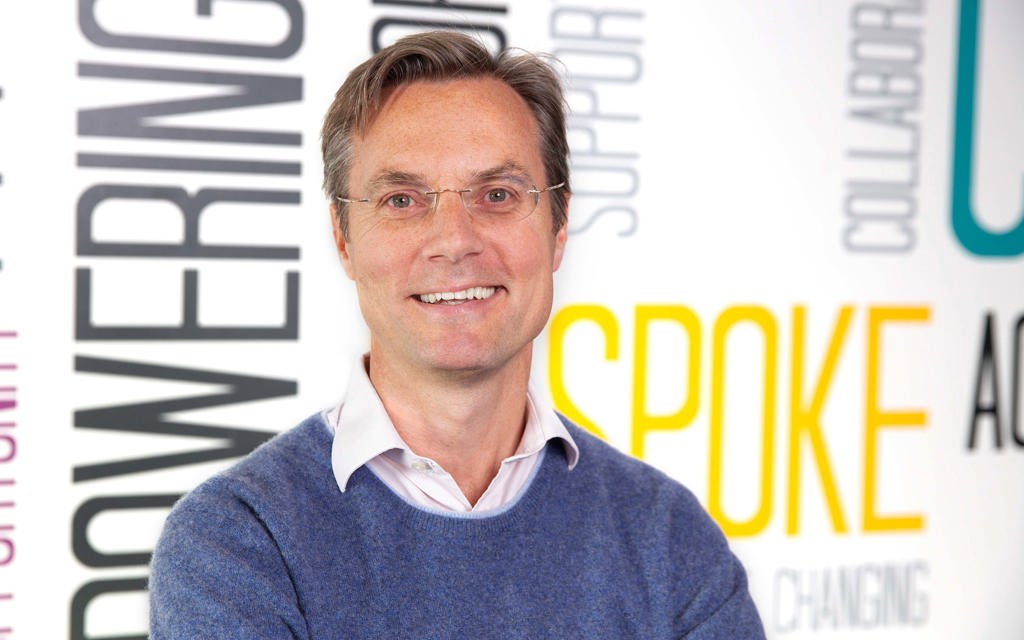 Philip is smiling and standing in front of a colourful background. 