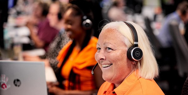 A lady in a bright orange is answering the telephone using a headset and smiling.  