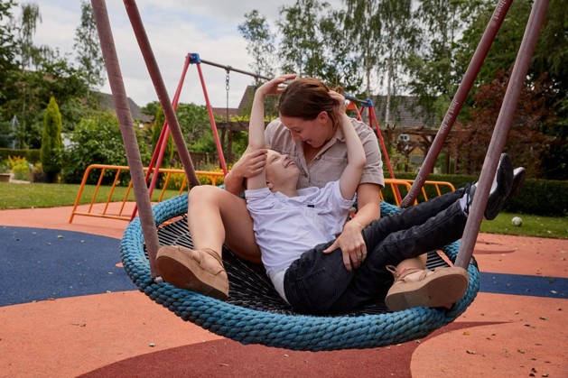 Becci and Lucas are sitting together in a swing, laughing and smiling at one another.