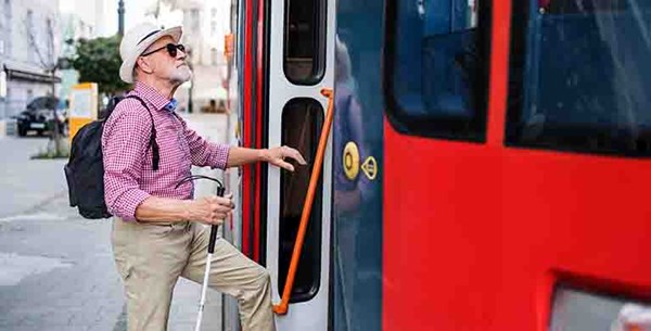 A man using a white cane climbing into the open door on a bus