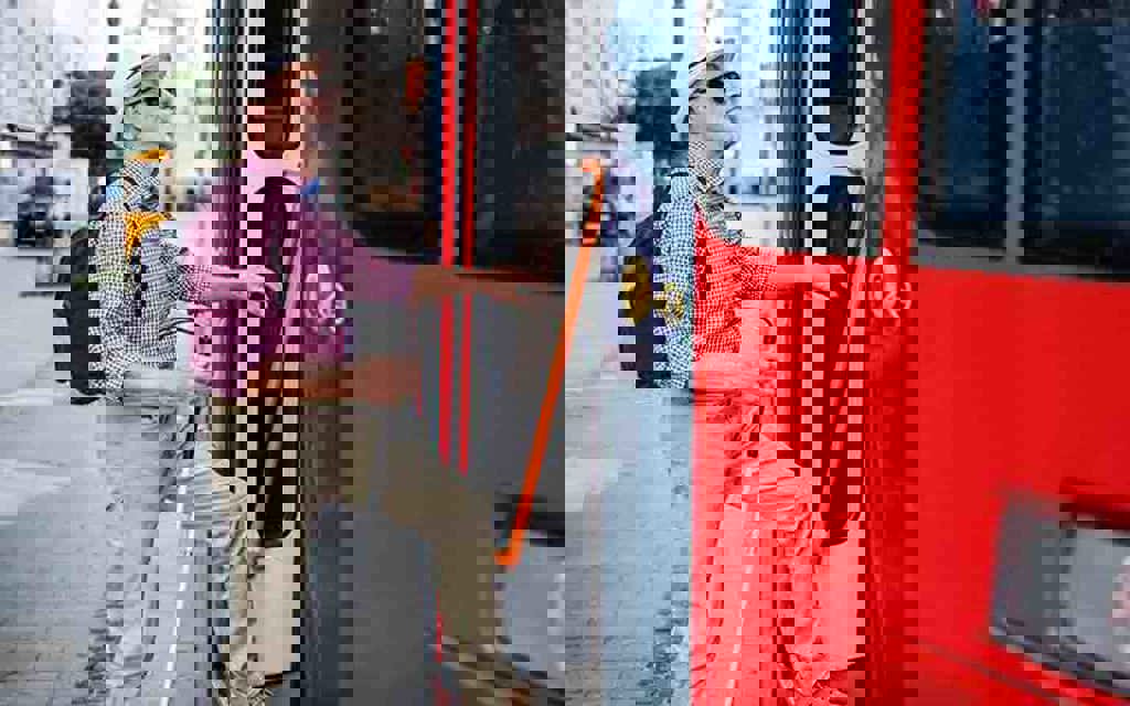 A man using a white cane climbing into the open door on a bus