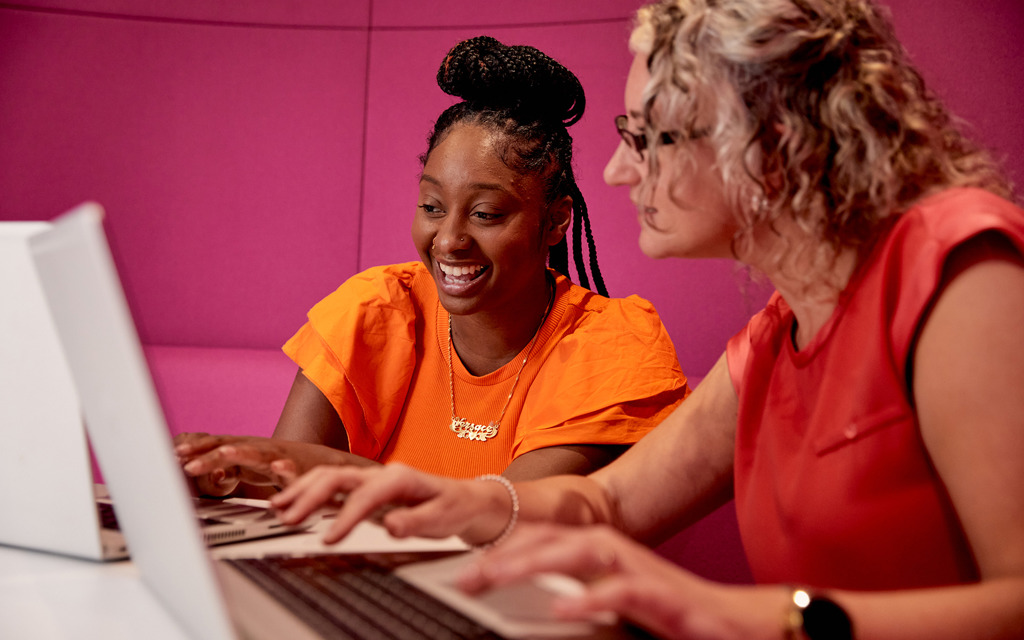 Two women sit at a table looking at a computer