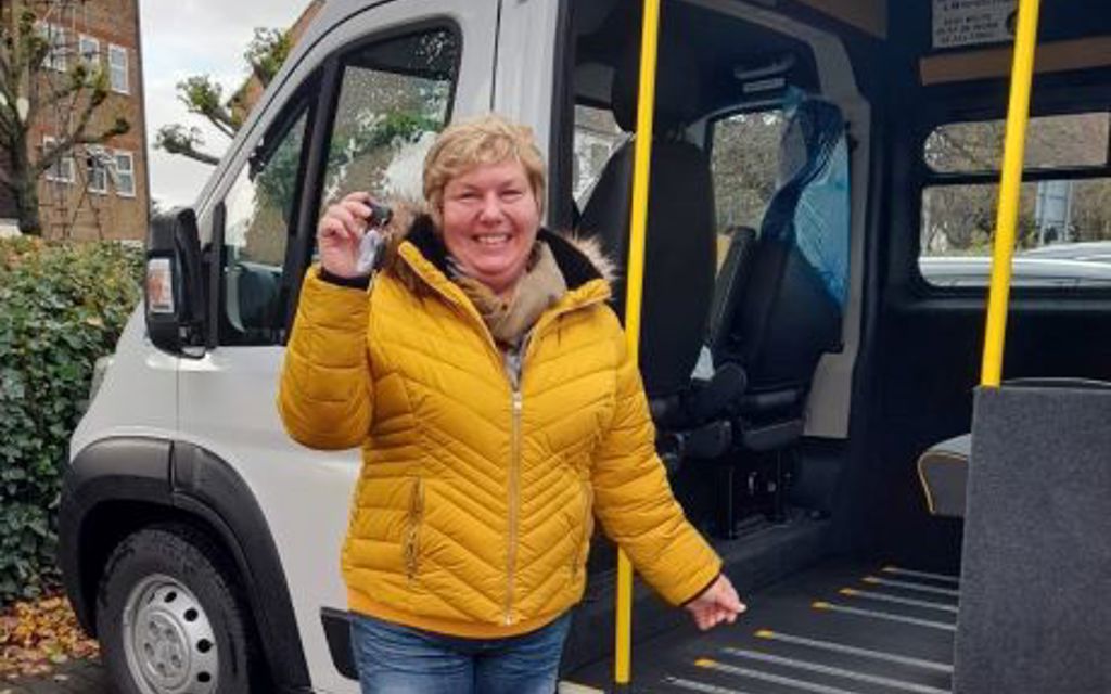 Lady smiling and proudly holding out the keys to a community transport vehicle, which is behind her.