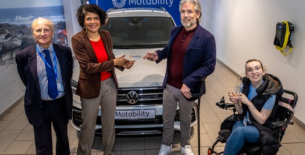 Chi Onwurah MP is handing over a glass key to Carl who is standing with his walking aid in front of his Motability, the Scheme vehicle. 