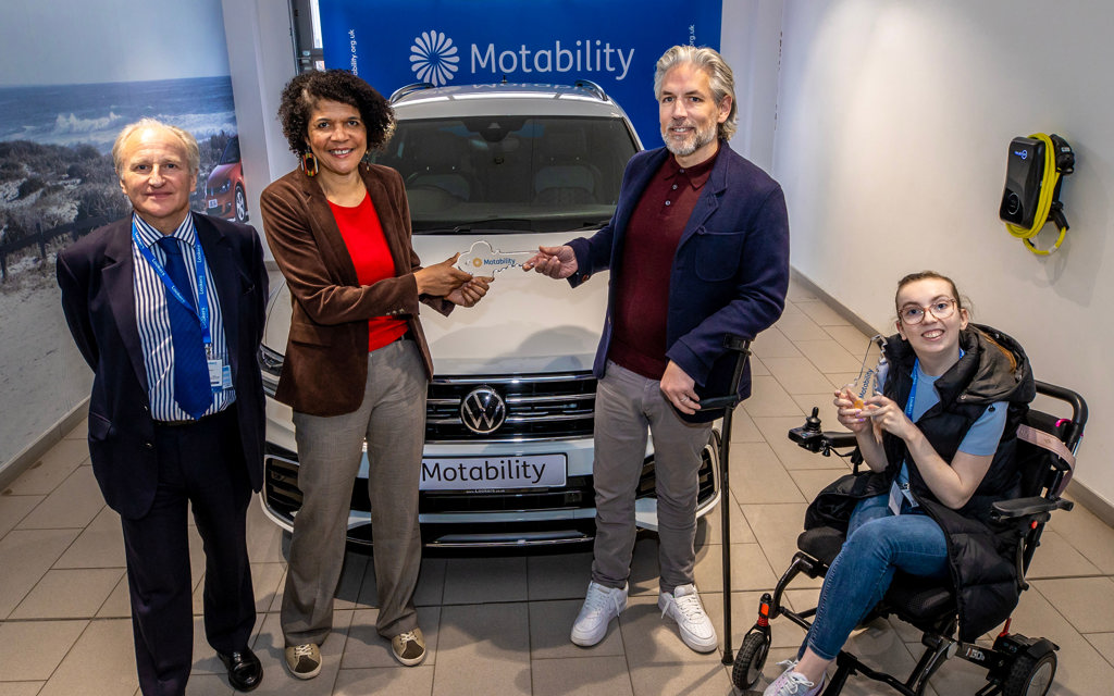 Chi Onwurah MP is handing over a glass key to Carl who is standing with his walking aid in front of his Motability, the Scheme vehicle.