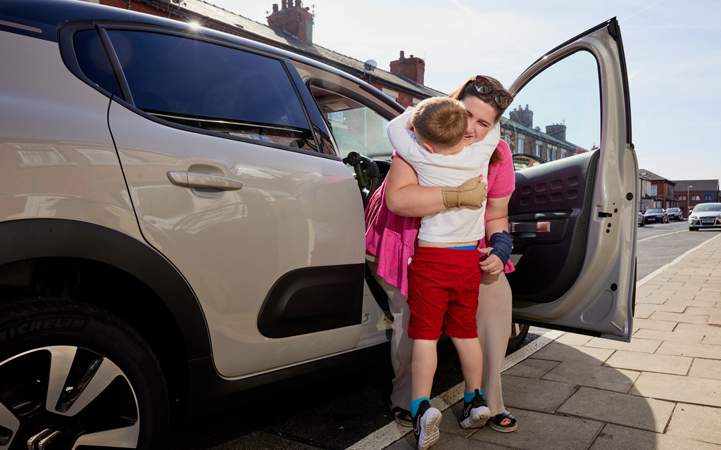 Jess is cuddling her son and smiling as she gets out of her car. 